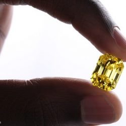 diamanti colorati diamante giallo, taglio a smeraldo tenuto tra due dita